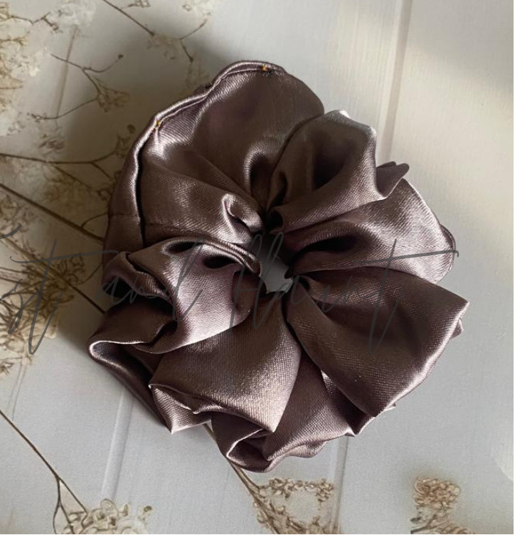 Brown satin scrunchie on a light wooden surface with dried flowers