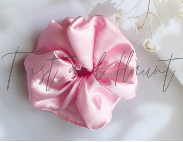 Pink scrunchie on a light surface with text and flowers in the background