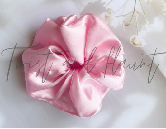 Pink scrunchie on a light surface with text and flowers in the background
