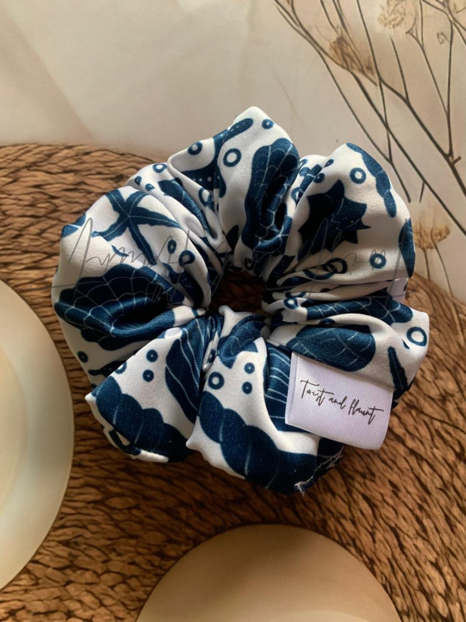 Twist and Flaunt Blue and white patterned scrunchie with a label on a wooden surface